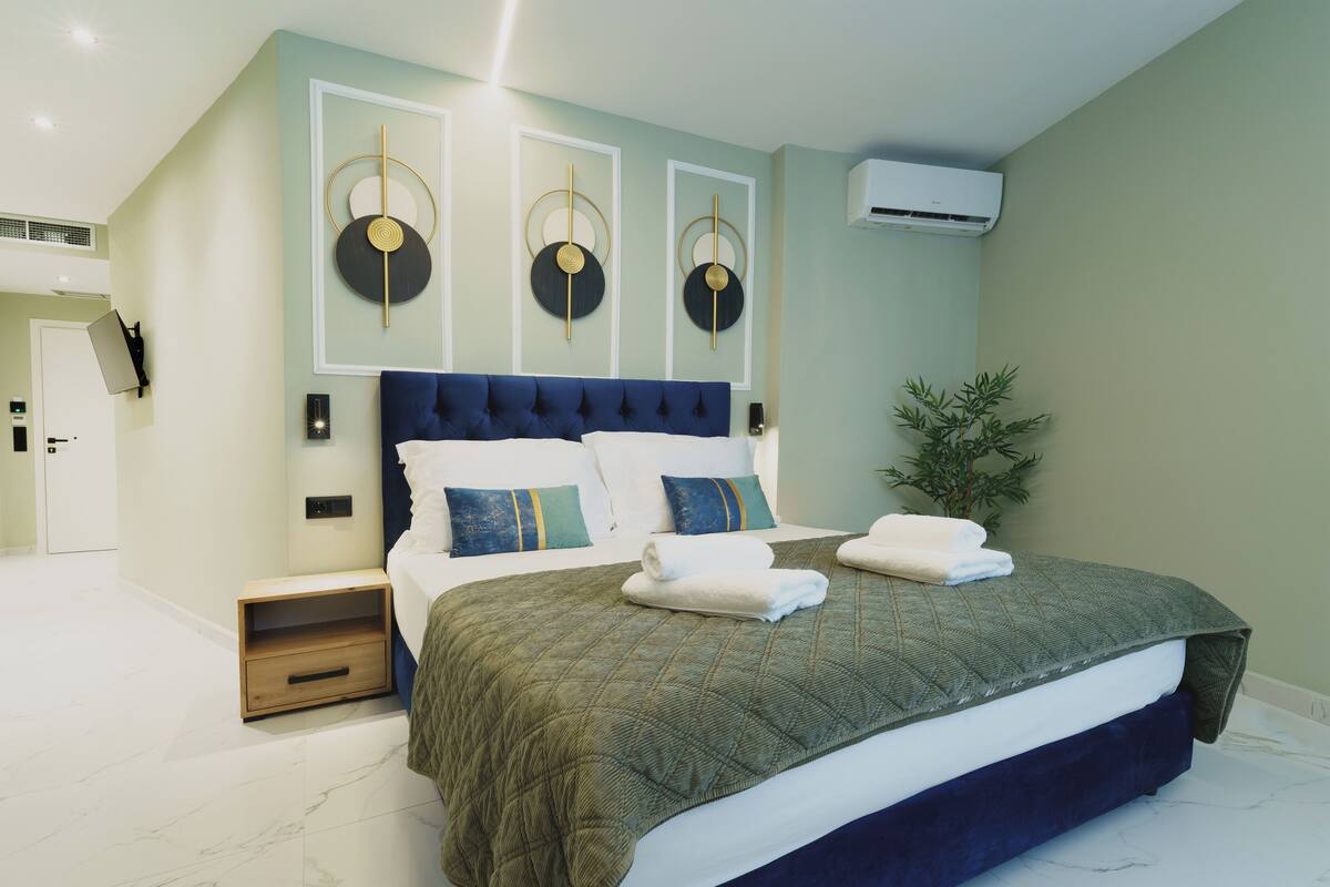 A modern bedroom with a large bed, a nightstand, a wall-mounted air conditioner, and a door.