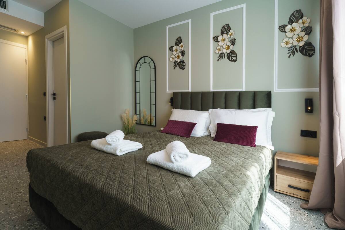A hotel room with a large bed, two pillows, a nightstand, a mirror, and a wall with decorative floral art.