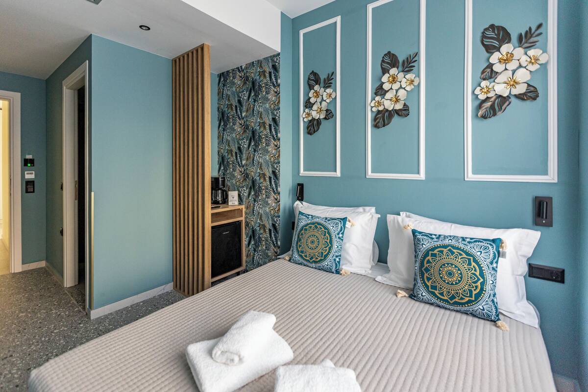 A hotel room with a bed, pillows, a coffee machine, a wardrobe, and a wall with floral decorations.