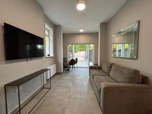 A modern living room with a flat-screen TV, a sofa, a coffee table, and a dining area with chairs and a table. - Spacious 5 Bedroom House in Acton Sleeps 10 (London)