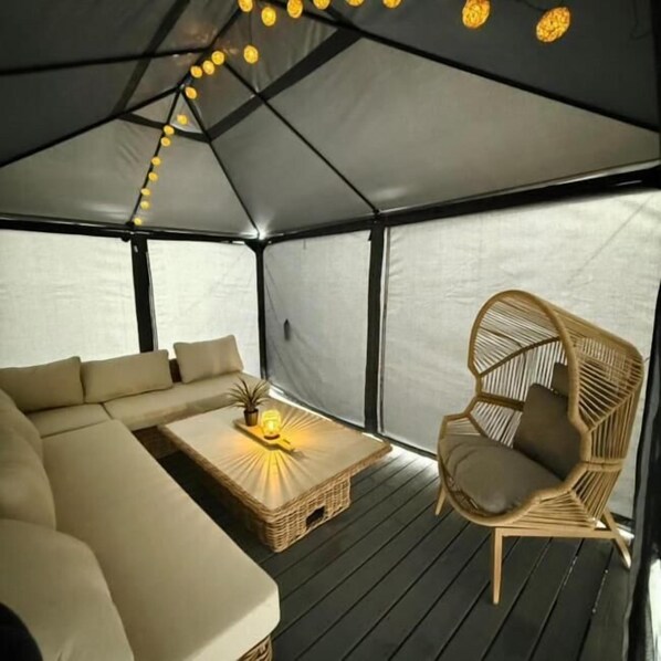 A tented room with a sofa, a wicker chair, and a small table with a lamp.