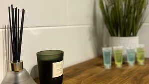 Una candela con l'etichetta 'SLEEP' su un'asse di legno, circondata da diffusori di canna e piccoli contenitori.