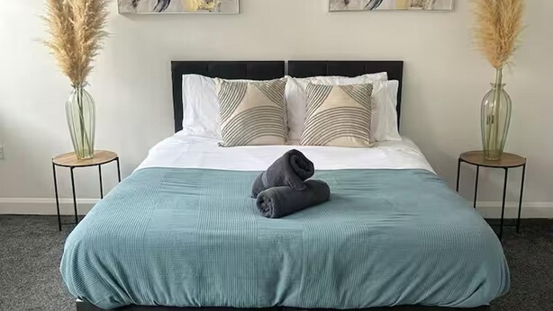 Un letto rifatto con cura, con una coperta color petrolio, due vasi decorativi con pampas e opere d'arte astratta alle pareti.