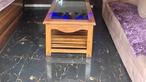 Una reception con una targa 'RECEPTION', un tavolo con piano in vetro, un divano trapuntato con una coperta viola e un murale raffigurante montagne.