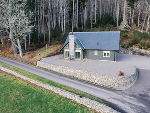 Een modern huis met een stenen fundering en een grijs dak, omringd door een bos.