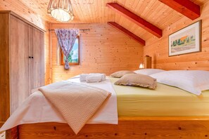 A wooden cabin bedroom with a bed, a wardrobe, a window with a curtain, and a painting on the wall. - Rural home in nature with jacuzzi, sauna and entertainment amenities (Mazin)