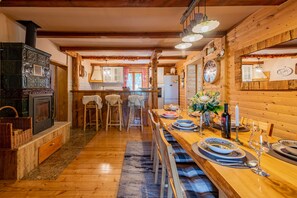 A rustic wooden interior with a long dining table set for a meal, a fireplace, and a kitchen area visible in the background. - Rural home in nature with jacuzzi, sauna and entertainment amenities (Mazin)