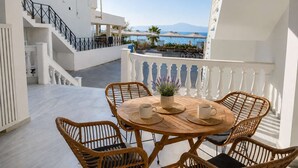 Ein Balkon mit Korbstühlen und einem Tisch, mit Blick auf einen Pool und eine gebirgige Landschaft.