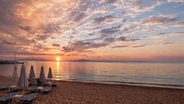 Ein Strand mit Liegestühlen und Sonnenschirmen, ein Sonnenuntergang und ruhiges Wasser.