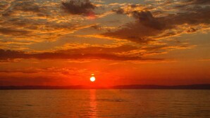 Ein Sonnenuntergang über einem ruhigen Meer mit sichtlichem Horizont und weiter Küste.