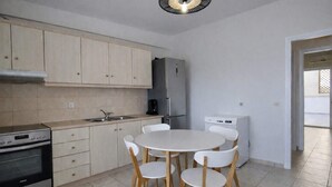 Eine kompakte Küche mit Essbereich, mit hellen Holzschränken, einem Einbauofen, einem Kühlschrank und einer Kaffeemaschine.
