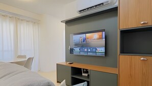 Una habitación de hotel moderna con una televisión de pantalla plana montada en una pared oscura, un mueble de madera y una cama con una manta gris.