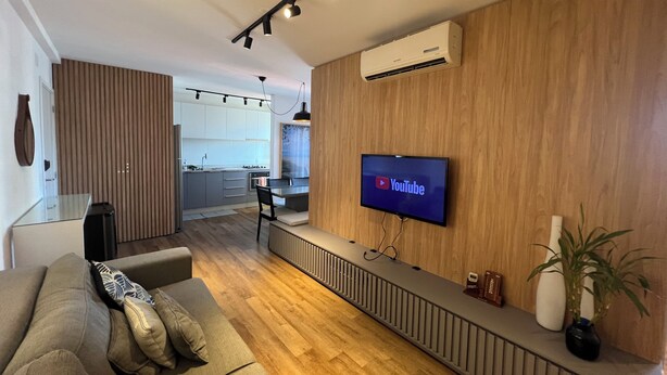 Een moderne woonkamer met een bank, een aan de muur bevestigde televisie en een keuken op de achtergrond.