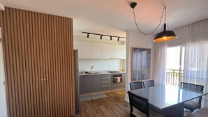 Een moderne keuken met witte kasten, een houten scheidingswand en een eethoek met een glazen tafel en stoelen.
