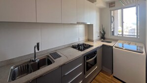 Een moderne keuken met witte kastjes, een roestvrijstalen spoelbak, een gasfornuis, een oven en een geïntegreerde vaatwasser.