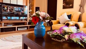 A living room with a television, a blue vase with flowers, a yellow armchair, and a coffee table.