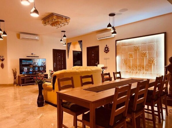 Un vaste espace de vie comprenant un grand canapé, une table à manger et des chaises. Un téléviseur à écran plat est fixé au mur, ainsi qu’un panneau décoratif.