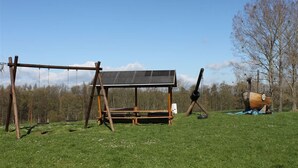 A wooden swing set, a covered seating area, and a decorative wooden boat in a grassy field. - Vacation apartment at Sonnenstein (Holungen)