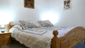 A neatly made bed with a wooden headboard, a bedside table with a lamp, and two framed pictures on the wall. - Vacation apartment at Sonnenstein (Holungen)