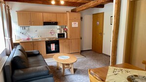 A compact living space with a kitchenette, a sofa, a dining table, and a wooden ceiling. - Vacation apartment at Sonnenstein (Holungen)
