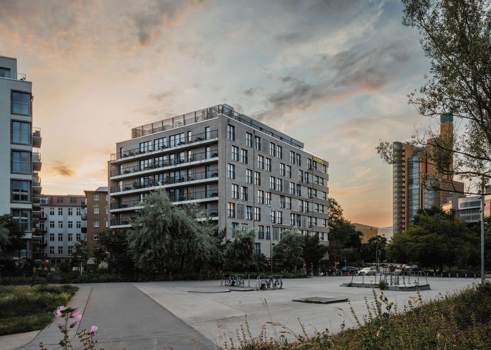 A multi-story building with a modern architectural design, surrounded by greenery and other buildings.