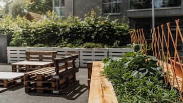 Un espacio al aire libre con bancos y mesas de madera, rodeado de vegetación y una cerca blanca.