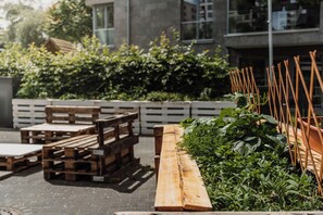 Ett utomhusområde med sittplatser, bestående av träbänkar och bord, omgivet av grönska och ett vitt staket.