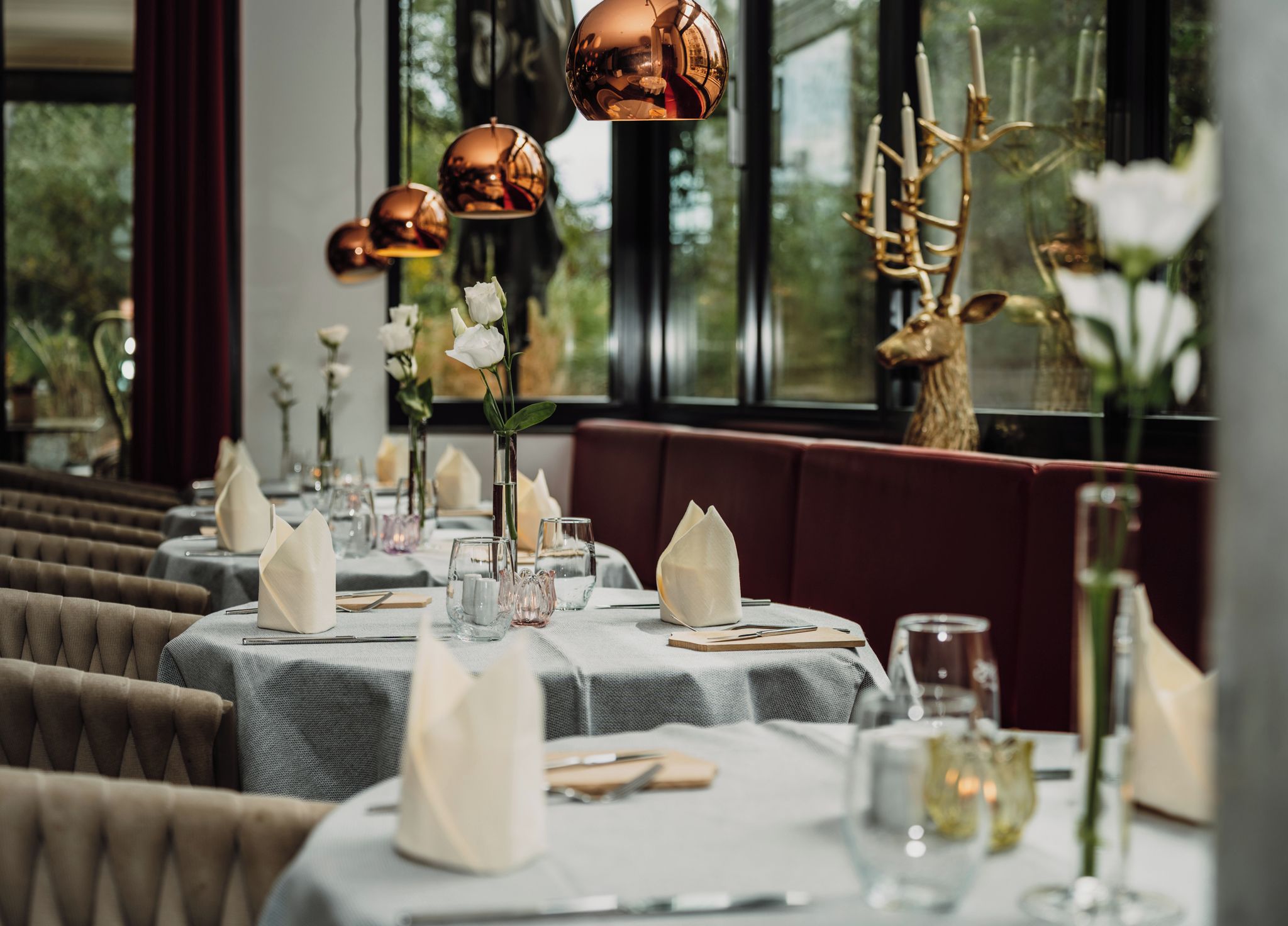 A restaurant setting with round tables, white napkins, and a decorative deer head.