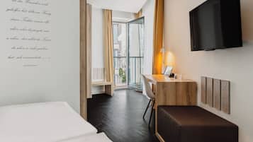 Habitación de hotel con cama, escritorio con ordenador portátil, televisor montado en la pared y vista a la ciudad por la ventana.
