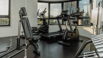 A gym with cardio machines, weightlifting equipment, and large windows offering city views.