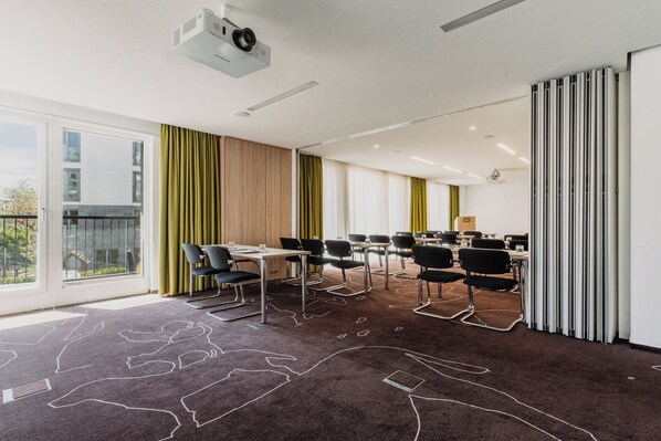 A conference room with a projector, multiple tables, chairs, and a view of the outdoors. - Grimms Potsdamer Platz (Berlin)