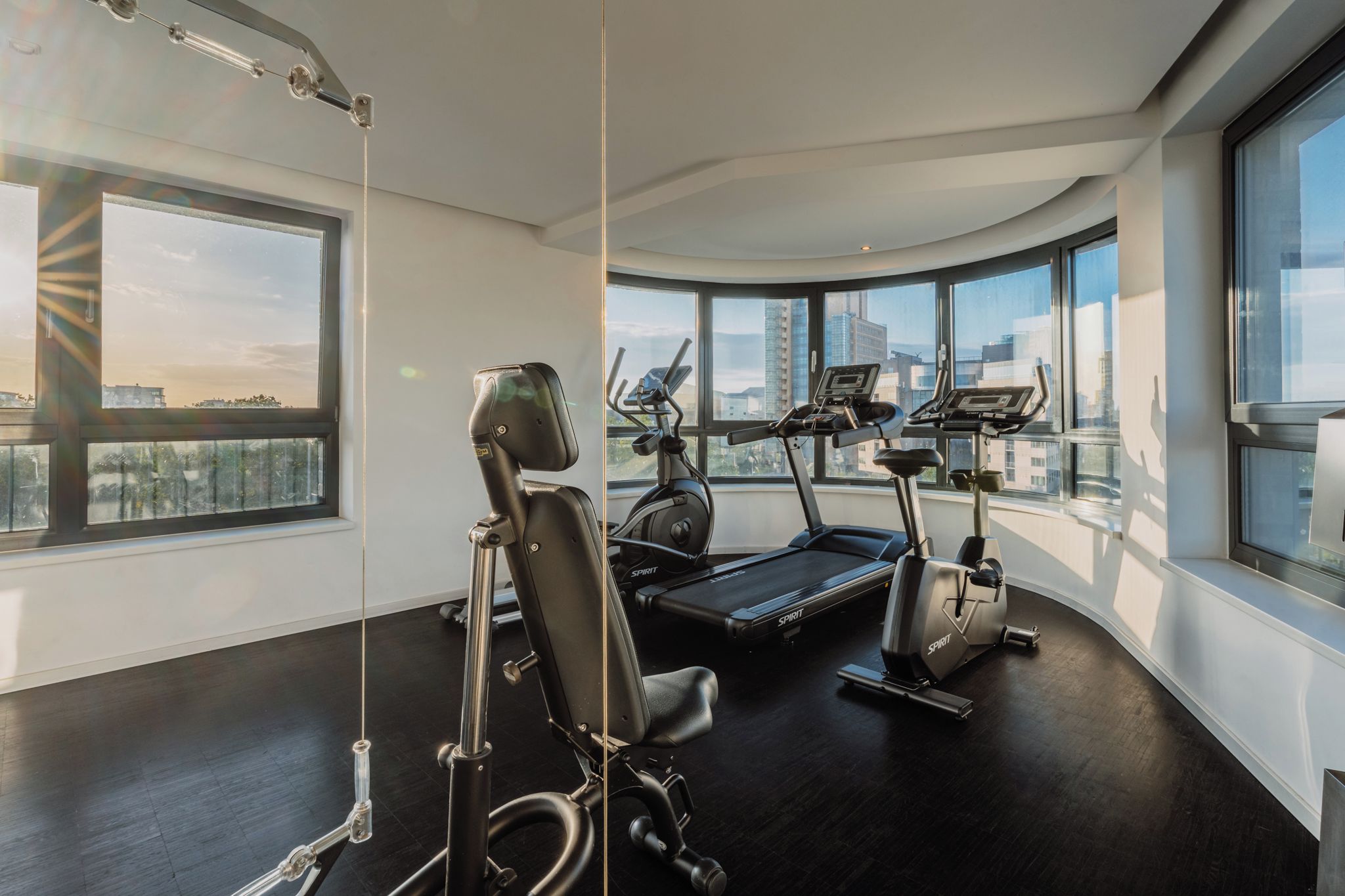 A modern gym with exercise equipment, large windows, and a city view.