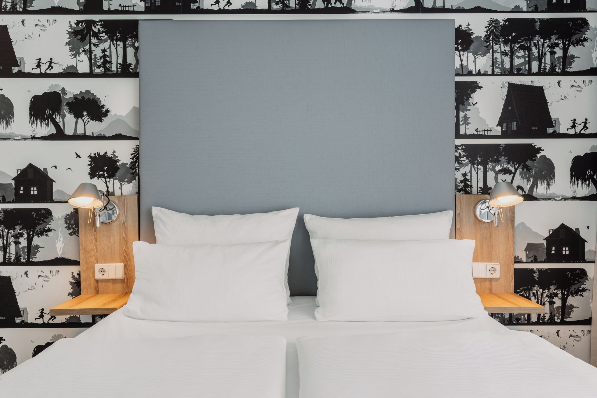 Ein Doppelbett mit weißen Bettwäsche, zwei Nachttischlampen und eine Wand mit Wandpapier mit Naturmotiv.