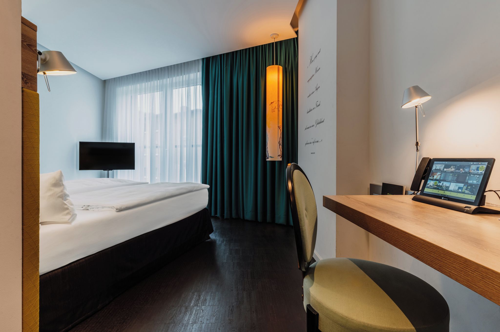 Una habitación de hotel con una cama, un escritorio con una computadora, una silla, un televisor y una pared con cortina.