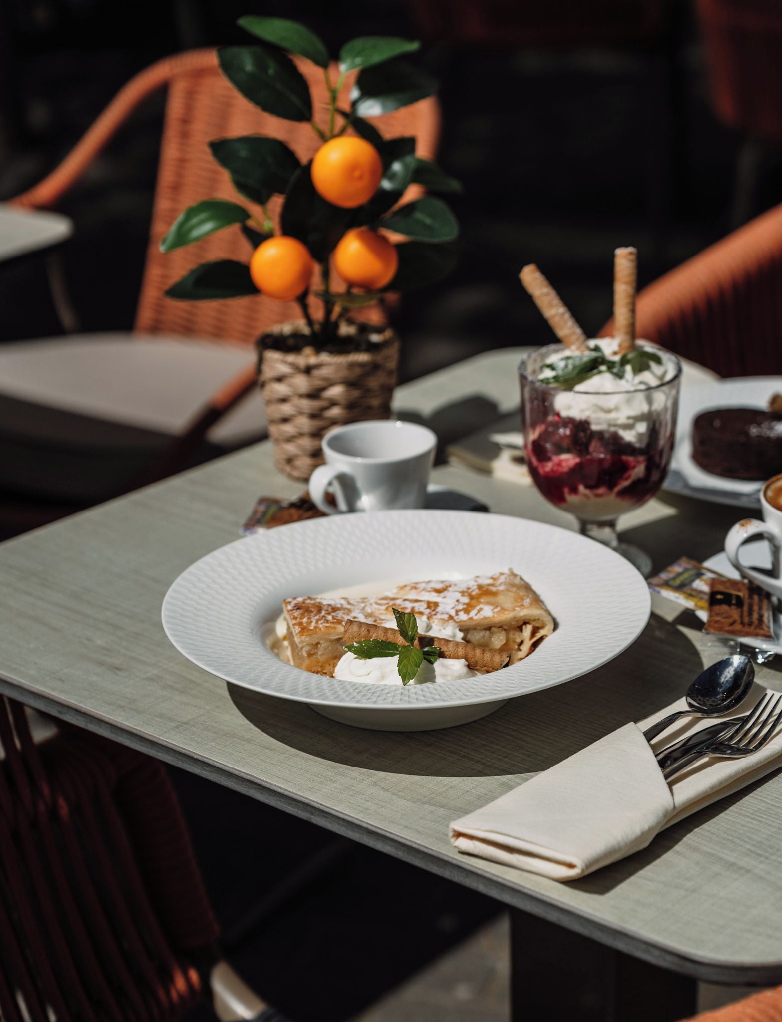 A table with a plate of food, a glass of drink, and a small plant with oranges.