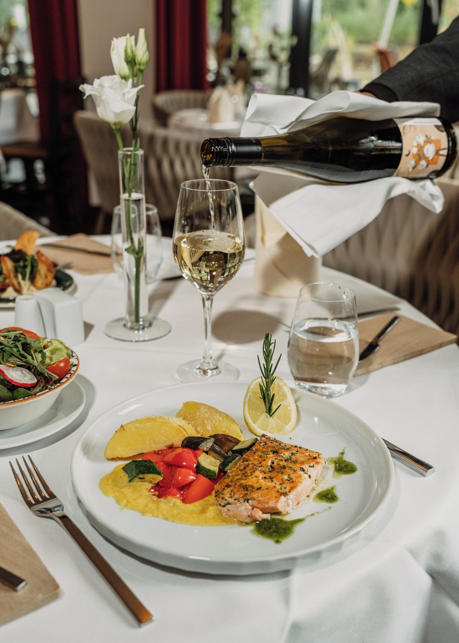 Une table à manger avec une assiette de nourriture, un verre d’eau et une bouteille dont on verse le contenu dans un verre.