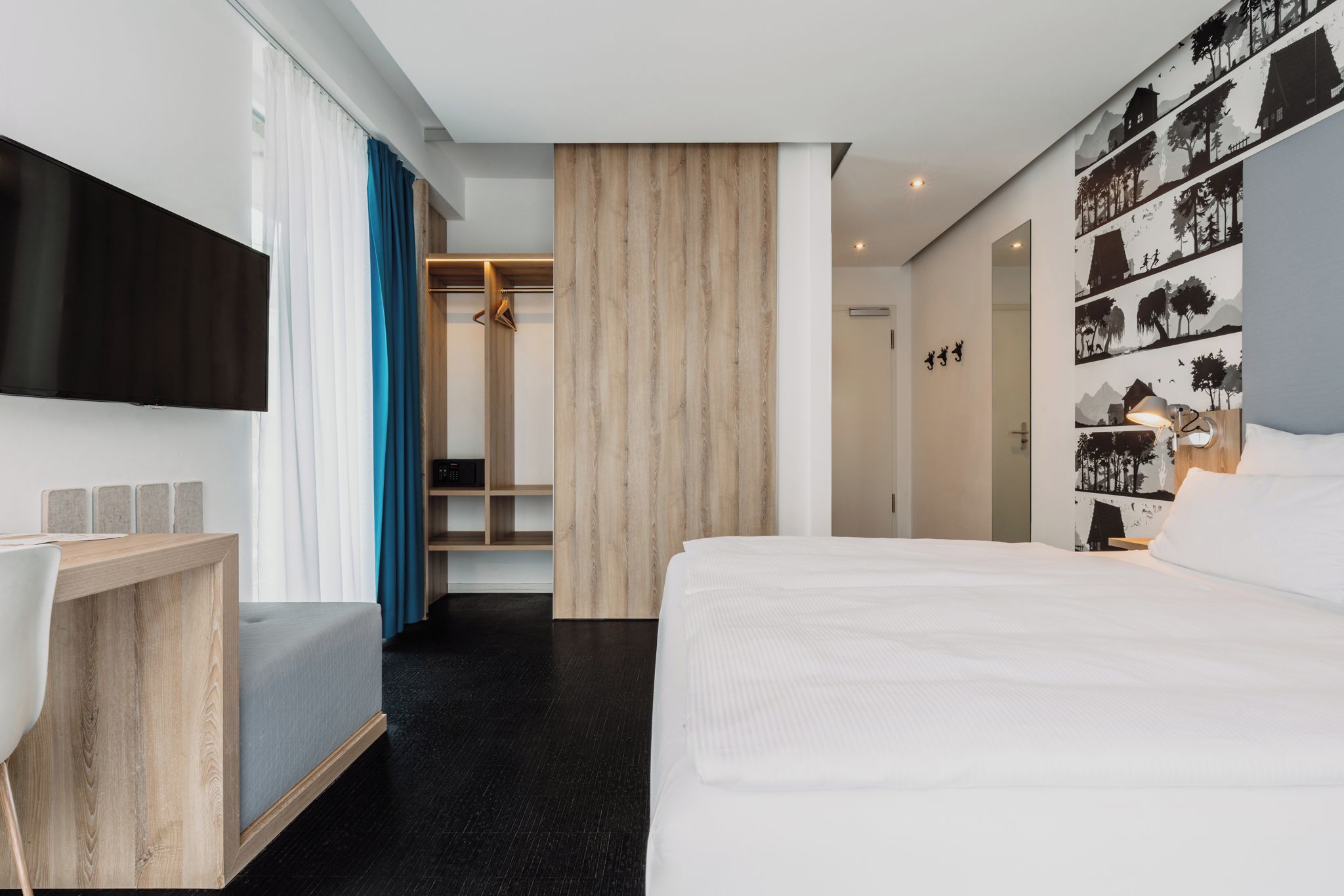 Ein modernes Hotelzimmer mit einem großen Bett, einem Schreibtisch, einem Kleiderschrank und einem Fernseher.