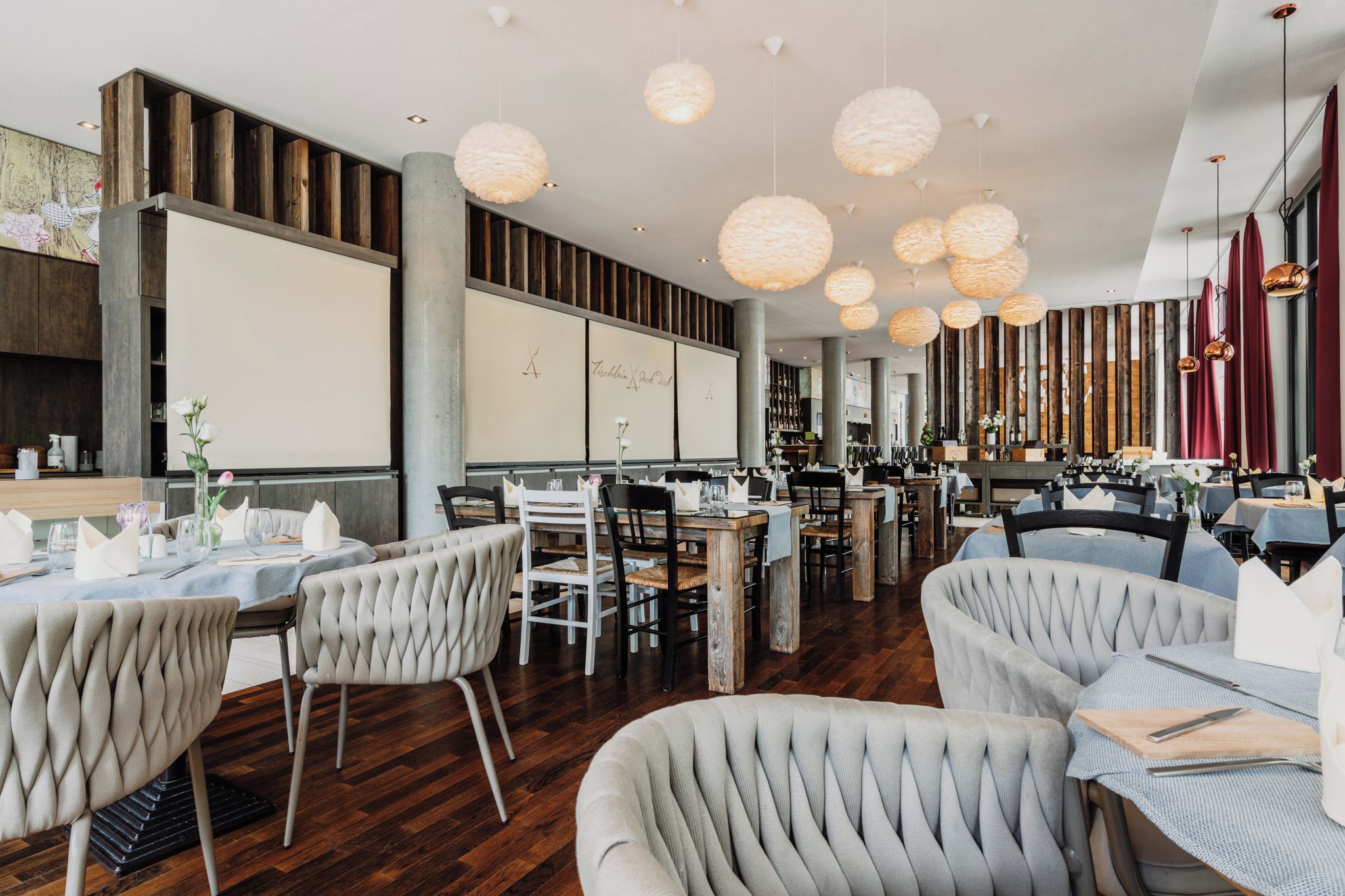 Een restaurantinterieur met houten lambrisering, ronde hanglampen en beklede stoelen.