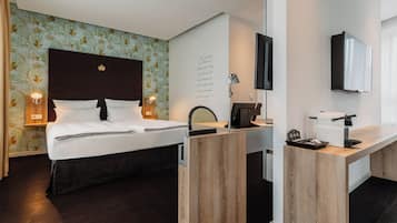 A hotel room with a bed, bedside lamps, a desk with a computer, a flat-screen TV, and a wall-mounted TV.