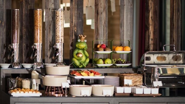 Ein reichhaltiges Buffet mit verschiedenen Speisen, darunter Obst, Gemüse und Gebäck, präsentiert auf einer Theke, auf der eine dekorative Froschfigur steht.