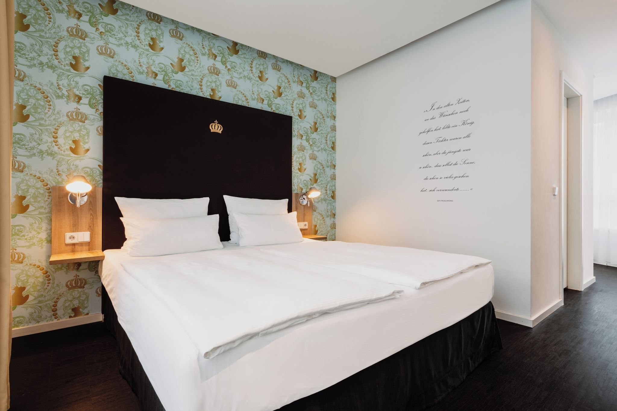 A neatly made bed with white linens in a hotel room with patterned wallpaper and a dark headboard.