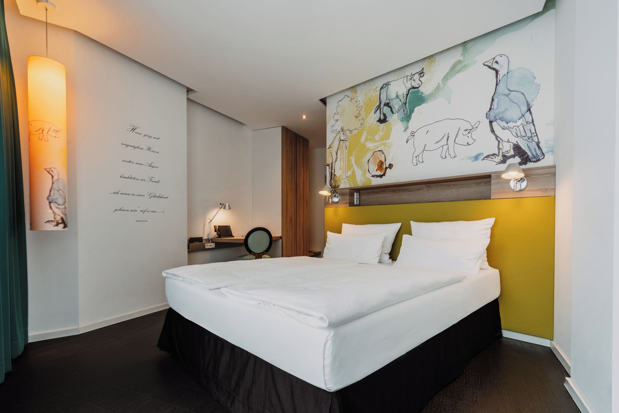 A hotel room with a bed, a wall-mounted artwork, a bedside lamp, and a mirror.