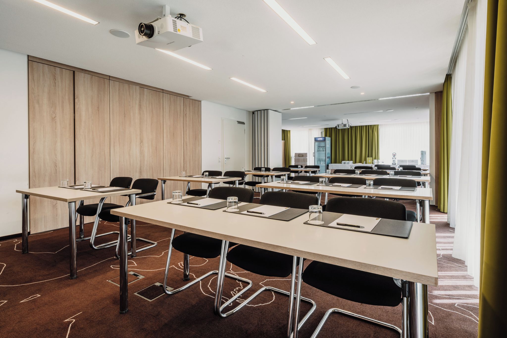 Un salón de conferencias con mesas, sillas, un proyector y un amplio ventanal con cortinas.