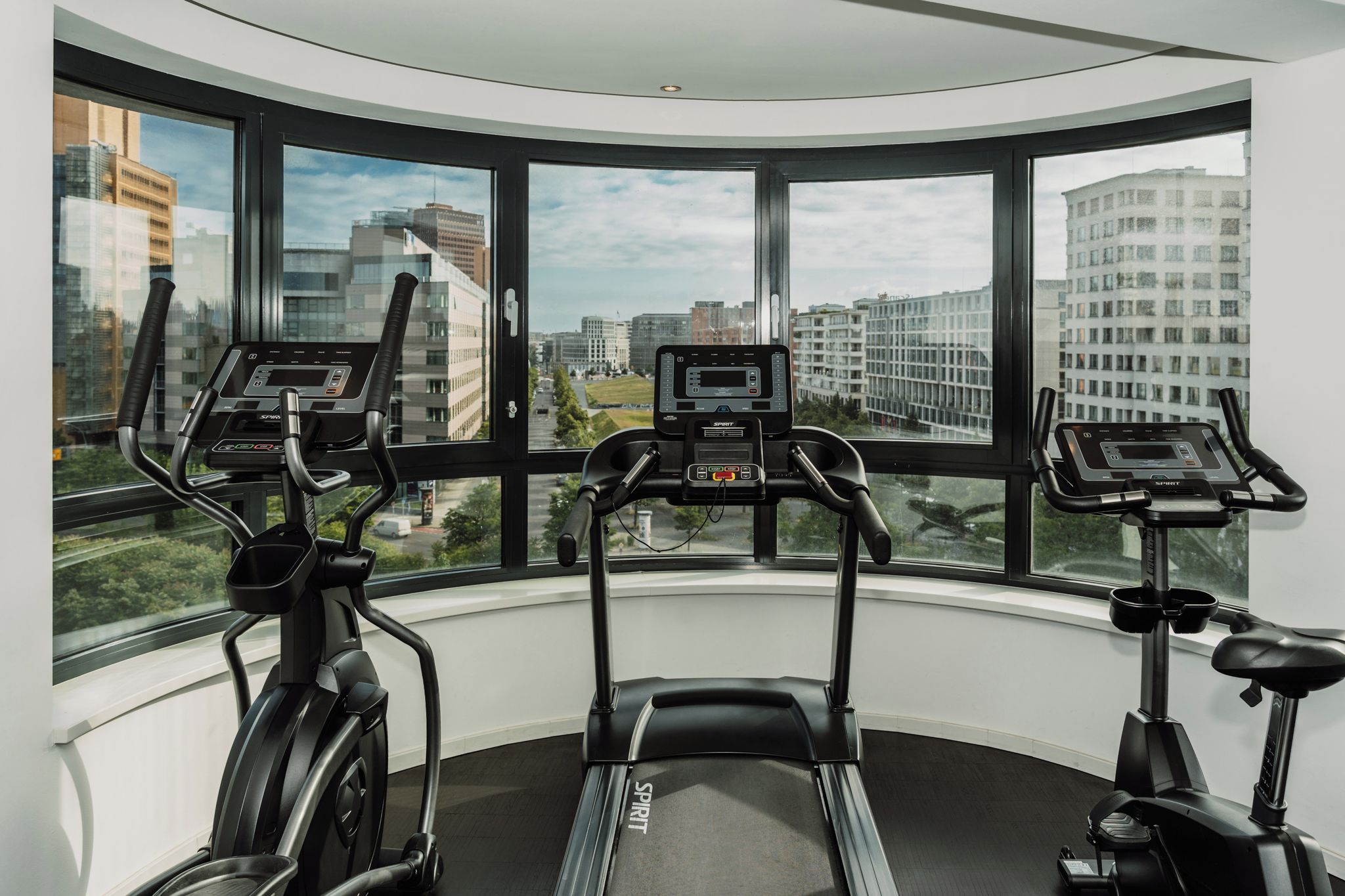 A gym with three treadmills, a large window with a city view, and a curved ceiling.