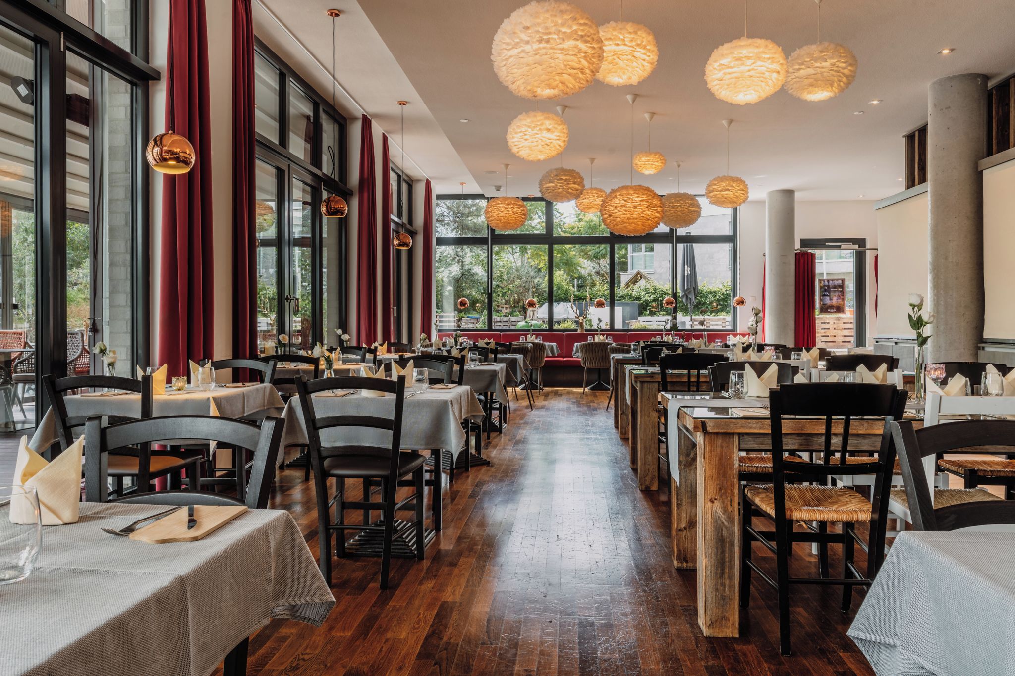 Interior de restaurante con varias mesas, sillas y lámparas esféricas colgantes.