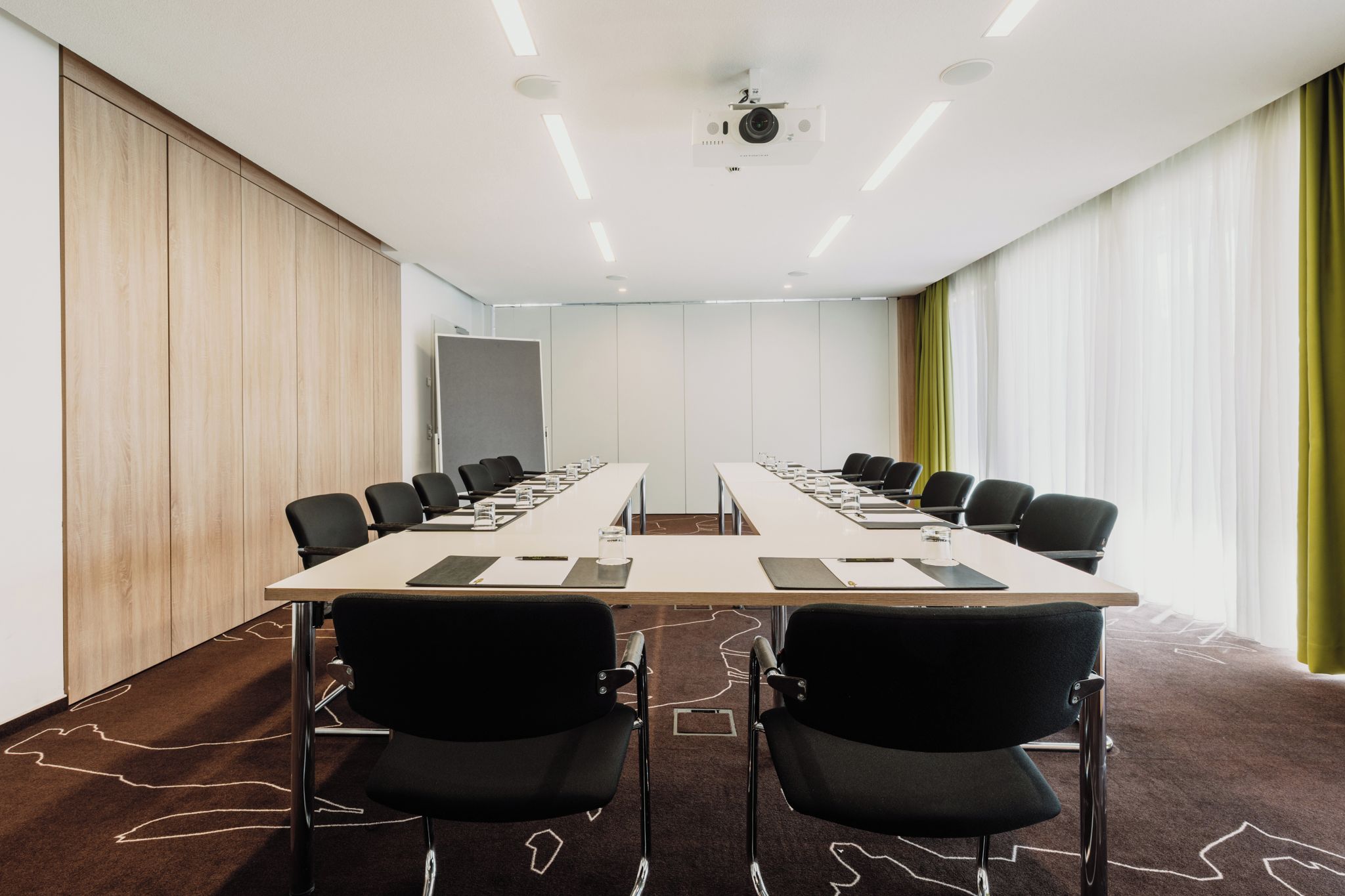 Een vergaderruimte met een lange tafel, zwarte stoelen en een projecteerder aan het plafond.