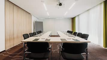 Een vergaderruimte met een lange tafel, zwarte stoelen en een projecteerder aan het plafond.