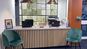 Un comptoir d’accueil avec deux chaises vertes, une fenêtre donnant sur des arbres et un panneau indiquant : « Nous revenons bientôt ».