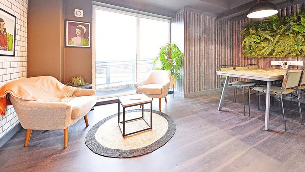 Un salon moderne comprenant un canapé, un fauteuil, une table basse et une table à manger avec des chaises. Une grande fenêtre laisse entrer la lumière naturelle et offre une vue sur l’extérieur.