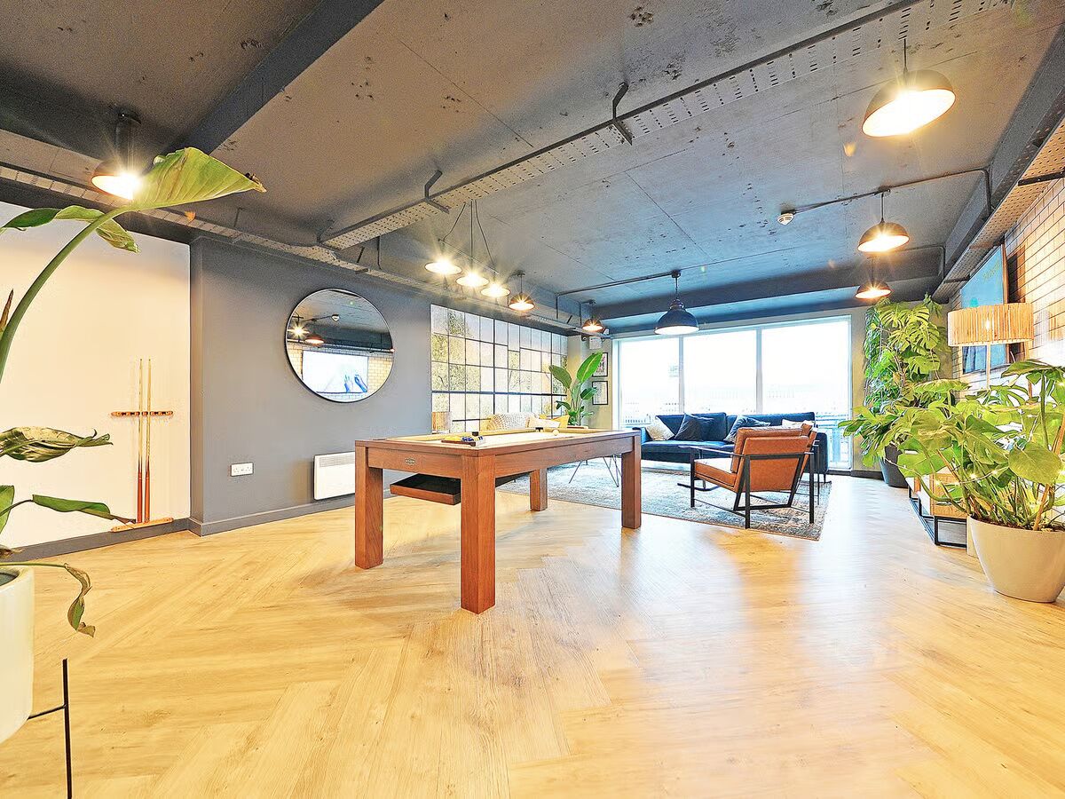 A spacious room with a wooden floor, a pool table, a sofa, and several potted plants.